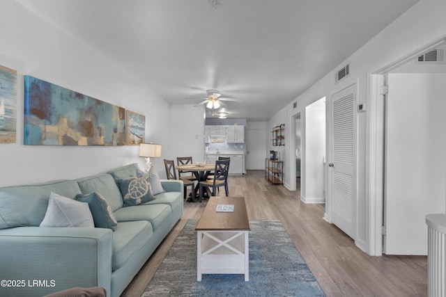 living room featuring light wood finished floors, visible vents, and a ceiling fan