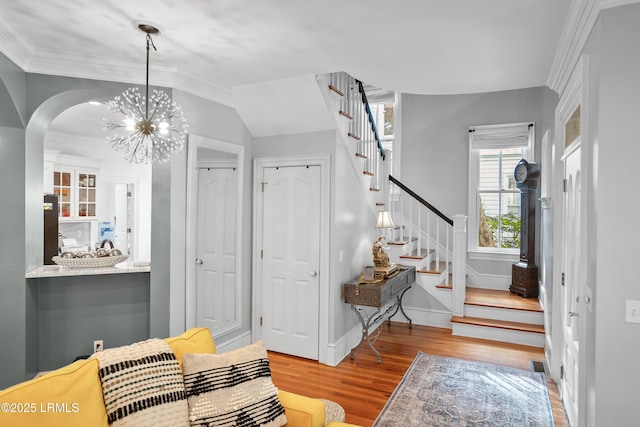 foyer featuring crown molding, an inviting chandelier, light wood-type flooring, baseboards, and stairs