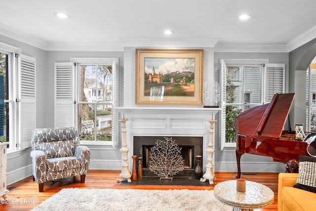 living area featuring a fireplace with flush hearth, a healthy amount of sunlight, crown molding, and wood finished floors