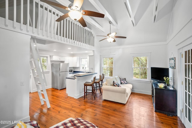 living area featuring hardwood / wood-style floors, ceiling fan, high vaulted ceiling, beamed ceiling, and baseboards