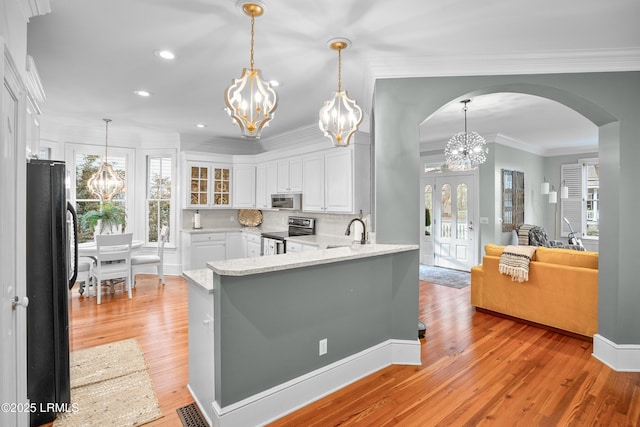 kitchen featuring arched walkways, white cabinets, glass insert cabinets, stainless steel appliances, and a notable chandelier