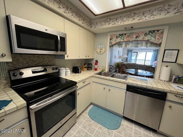 kitchen with sink, appliances with stainless steel finishes, tasteful backsplash, tile counters, and light tile patterned flooring