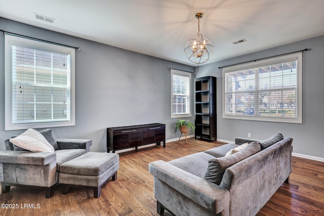 living area featuring baseboards, a notable chandelier, visible vents, and wood finished floors