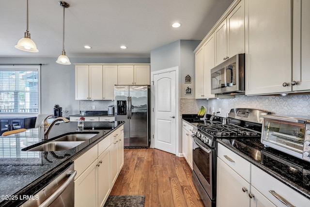 kitchen featuring wood finished floors, a sink, hanging light fixtures, appliances with stainless steel finishes, and dark stone countertops