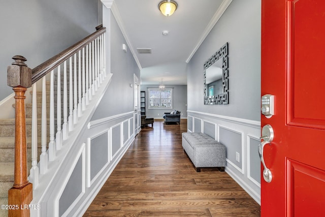 foyer entrance featuring stairs, crown molding, a decorative wall, and wood finished floors