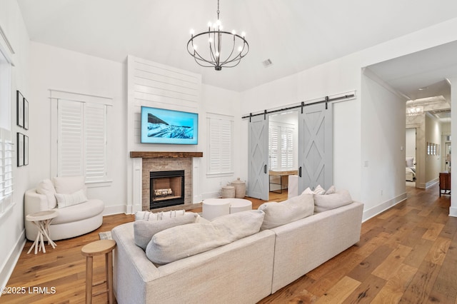 living room featuring a fireplace, wood-type flooring, a barn door, and a chandelier