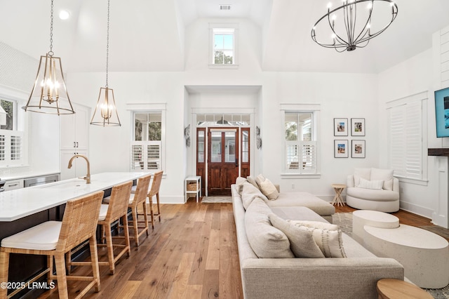 living room with a notable chandelier, a towering ceiling, sink, and light wood-type flooring