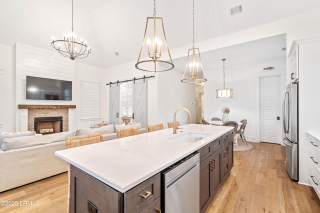 kitchen featuring sink, appliances with stainless steel finishes, a kitchen island with sink, white cabinets, and a barn door