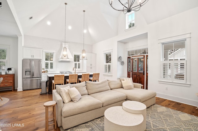 living room featuring high vaulted ceiling, sink, an inviting chandelier, and light wood-type flooring