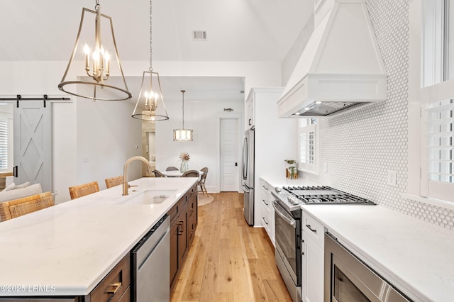 kitchen featuring appliances with stainless steel finishes, an island with sink, sink, a barn door, and custom range hood