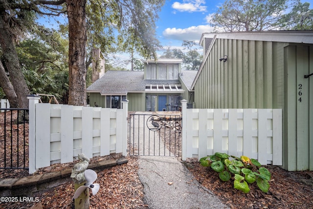 exterior space with a gate, roof with shingles, board and batten siding, and fence