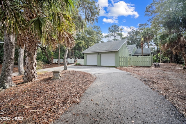view of side of home with fence, aphalt driveway, a shingled roof, and a garage