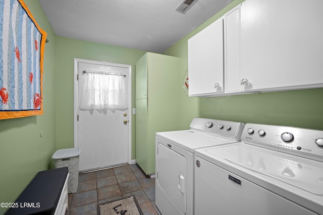 laundry area with washer and clothes dryer, a textured ceiling, cabinet space, stone finish floor, and visible vents