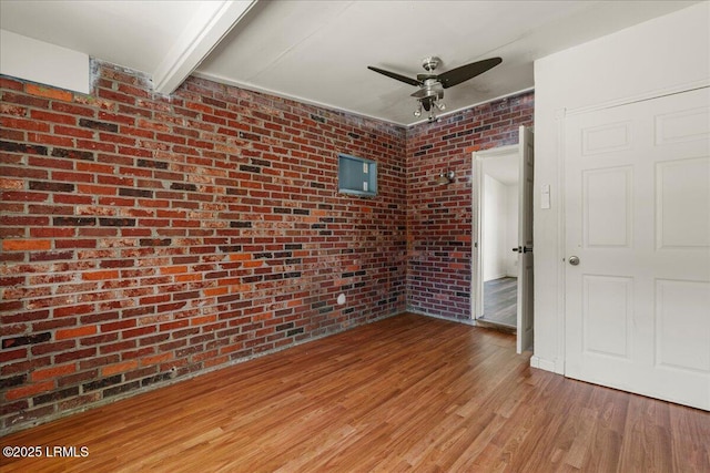 unfurnished bedroom featuring hardwood / wood-style flooring, ceiling fan, and brick wall