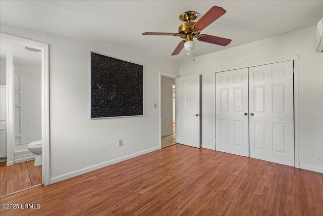 unfurnished bedroom featuring hardwood / wood-style flooring, ceiling fan, ensuite bathroom, a wall mounted air conditioner, and a closet