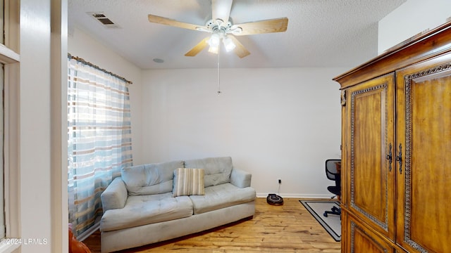 living room with a textured ceiling, ceiling fan, and light hardwood / wood-style flooring