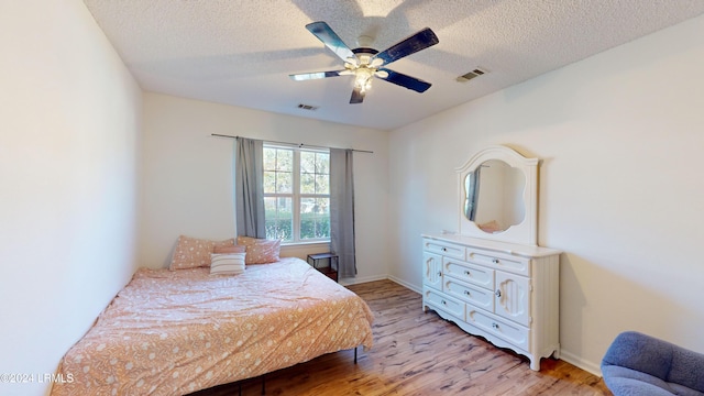 bedroom with a textured ceiling, ceiling fan, and light hardwood / wood-style floors