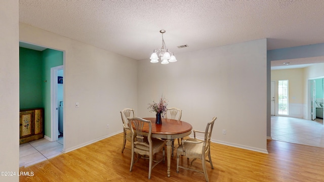 dining area featuring an inviting chandelier, light hardwood / wood-style floors, and a textured ceiling