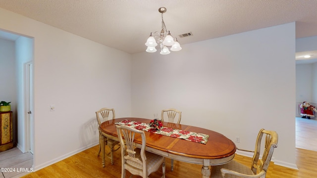 dining space with an inviting chandelier, a textured ceiling, and light wood-type flooring