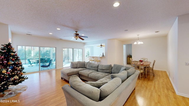 living room featuring ceiling fan with notable chandelier, light hardwood / wood-style flooring, and a textured ceiling