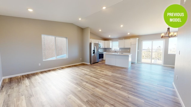 interior space with stainless steel fridge, a kitchen island, light hardwood / wood-style floors, an inviting chandelier, and white cabinetry