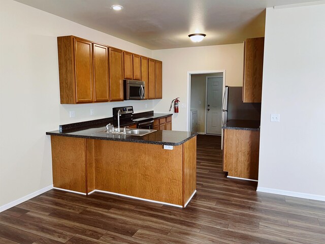 kitchen featuring dark hardwood / wood-style flooring, washer / clothes dryer, kitchen peninsula, stainless steel appliances, and dark stone countertops