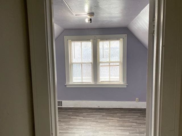 additional living space with light wood-type flooring, vaulted ceiling, and a textured ceiling