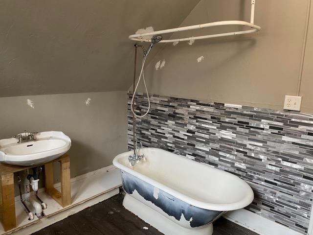 bathroom featuring lofted ceiling, a tub, sink, and decorative backsplash