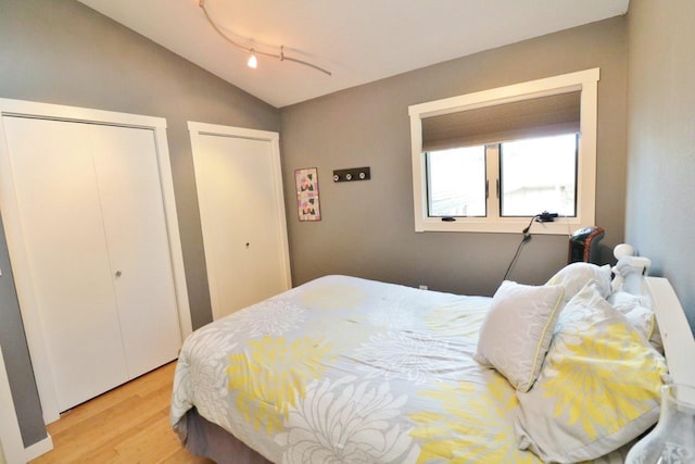 bedroom featuring light wood-type flooring, track lighting, vaulted ceiling, and multiple closets