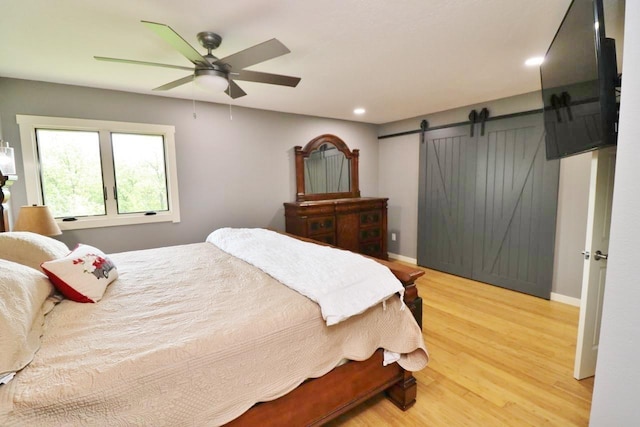 bedroom featuring a barn door, light hardwood / wood-style floors, and ceiling fan