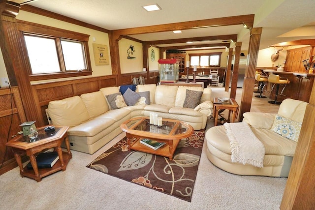 carpeted living room featuring beamed ceiling, wood walls, and ornamental molding