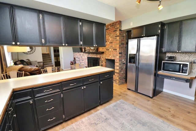 kitchen featuring kitchen peninsula, light hardwood / wood-style flooring, stainless steel refrigerator with ice dispenser, and a brick fireplace