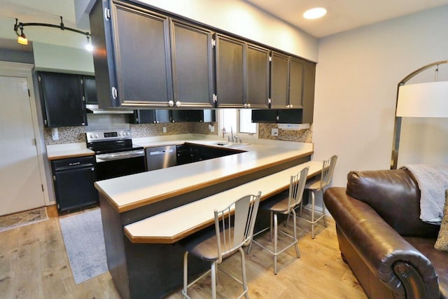 kitchen featuring decorative backsplash, appliances with stainless steel finishes, light wood-type flooring, kitchen peninsula, and a breakfast bar