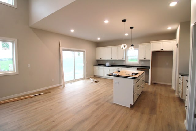 kitchen with light hardwood / wood-style floors, white cabinets, a kitchen island, and pendant lighting