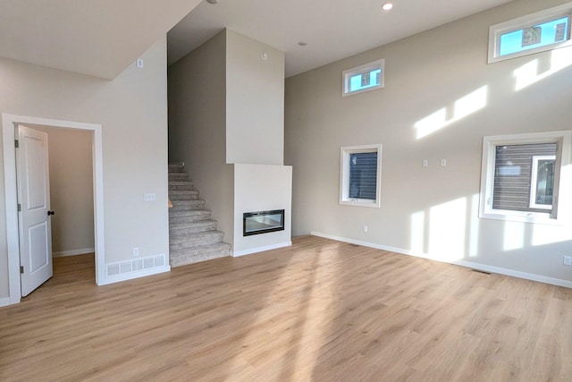 unfurnished living room with a towering ceiling, light wood-type flooring, and plenty of natural light