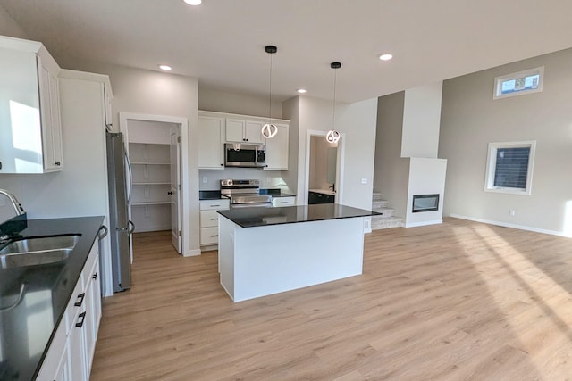 kitchen with appliances with stainless steel finishes, sink, a kitchen island, white cabinetry, and decorative light fixtures