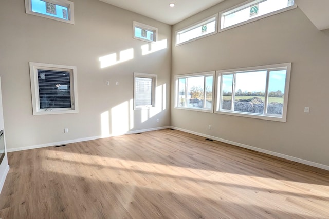 empty room with light hardwood / wood-style floors, a towering ceiling, and a wealth of natural light