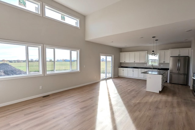 kitchen with stainless steel fridge, a kitchen island, white cabinetry, sink, and decorative light fixtures