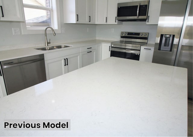 kitchen featuring sink, a kitchen island, stainless steel appliances, white cabinets, and light stone counters