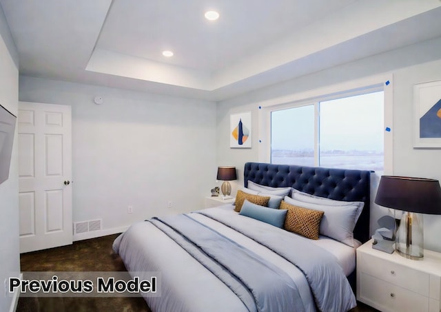 bedroom with dark colored carpet and a raised ceiling