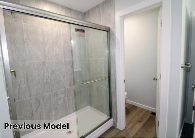 bathroom with a shower with shower door, hardwood / wood-style flooring, and toilet