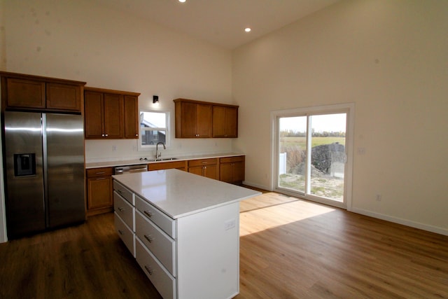 kitchen with high vaulted ceiling, stainless steel appliances, wood-type flooring, and a kitchen island