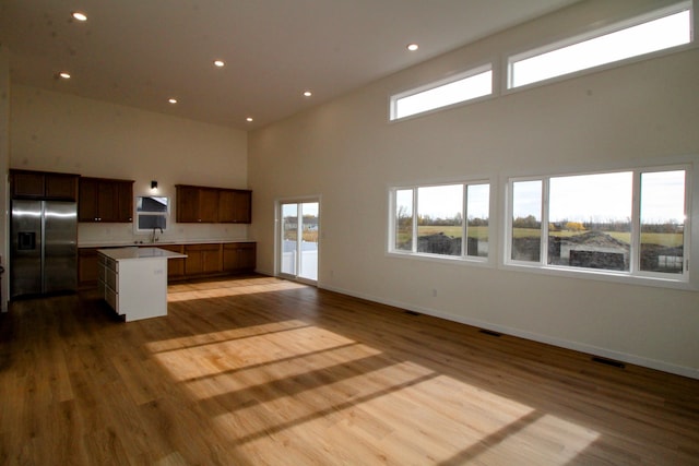 kitchen with a kitchen island, light hardwood / wood-style flooring, a towering ceiling, stainless steel refrigerator with ice dispenser, and sink