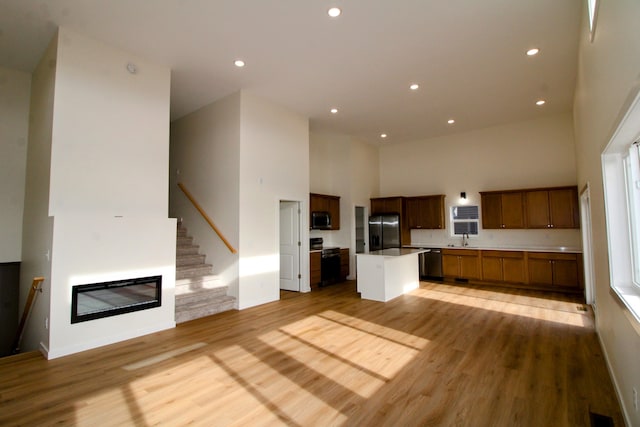 kitchen with sink, a center island, light hardwood / wood-style floors, stainless steel appliances, and a high ceiling