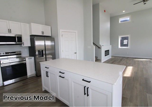 kitchen featuring a towering ceiling, a kitchen island, white cabinetry, stainless steel appliances, and dark wood-type flooring