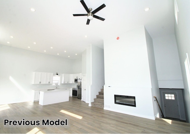 unfurnished living room featuring sink, a fireplace, ceiling fan, a high ceiling, and hardwood / wood-style flooring