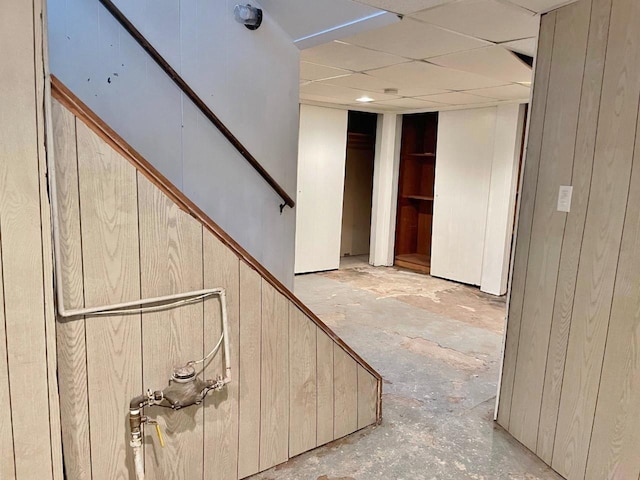 staircase featuring a drop ceiling, wood walls, and concrete floors