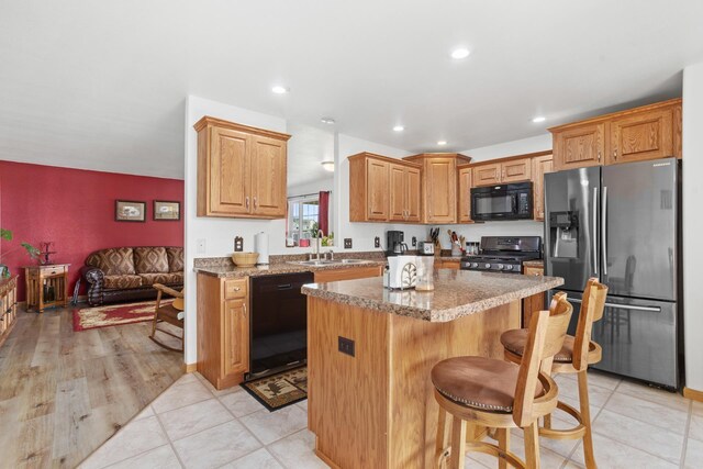 kitchen featuring light hardwood / wood-style flooring, a center island, black appliances, light stone countertops, and a kitchen breakfast bar