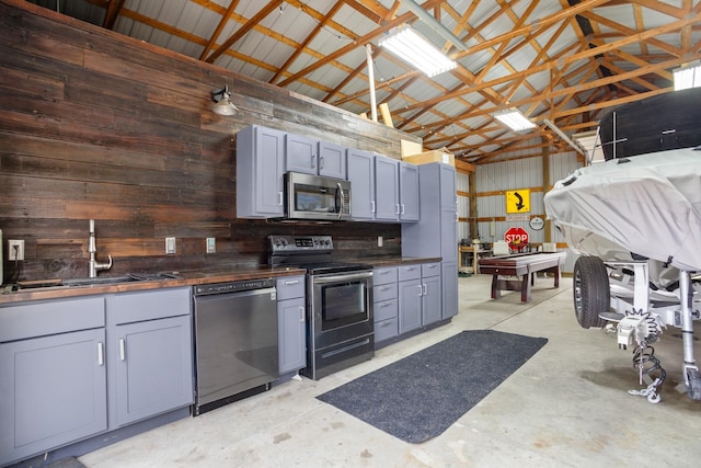 kitchen with gray cabinets, wood walls, appliances with stainless steel finishes, butcher block counters, and sink