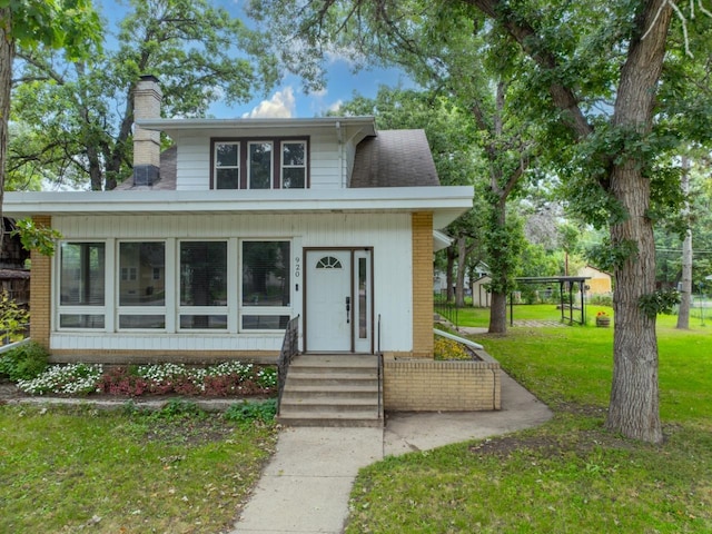 bungalow-style house featuring entry steps, brick siding, a chimney, and a front lawn